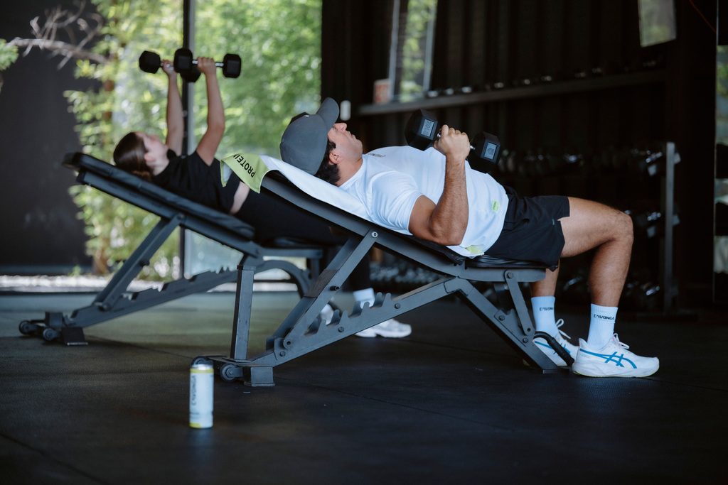 A  man and a woman working out on a bench with dumbbells. Photo credit Pexels